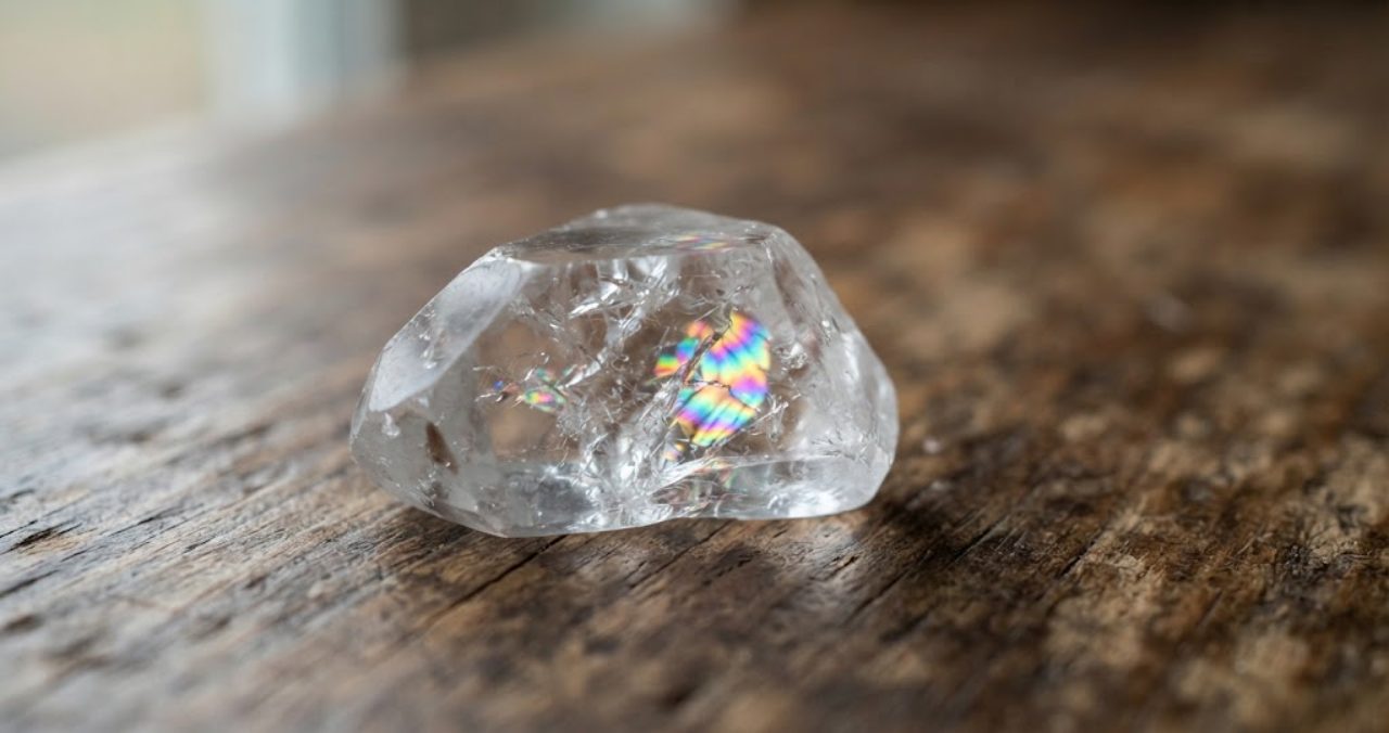 透明な水晶の原石の内部にあるひび割れに光が当たって虹色に輝いているレインボー水晶のクローズアップ写真